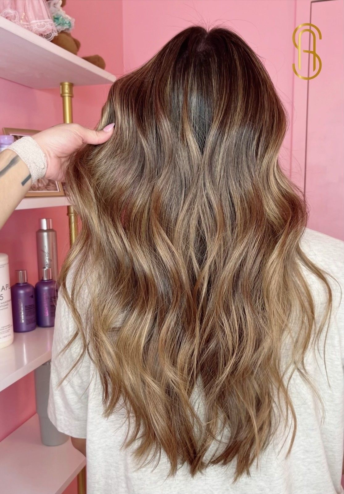 A woman with long brown hair is standing in front of a pink wall.