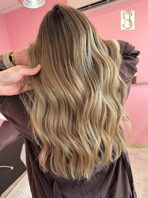 A woman with long blonde hair is standing in front of a pink wall.