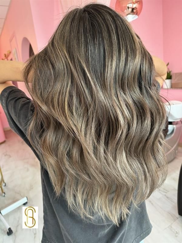 A woman with long wavy hair is standing in front of a pink wall.