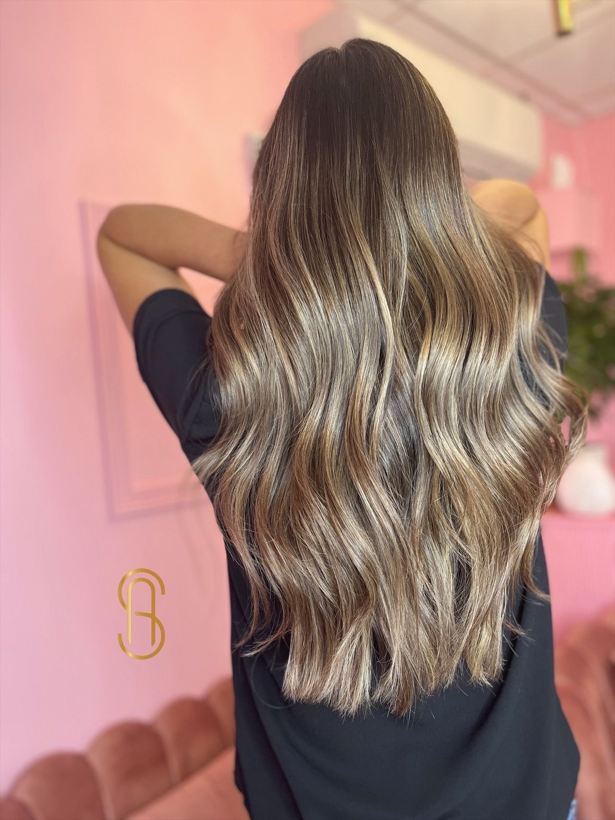 A woman with long brown hair is standing in front of a pink wall.