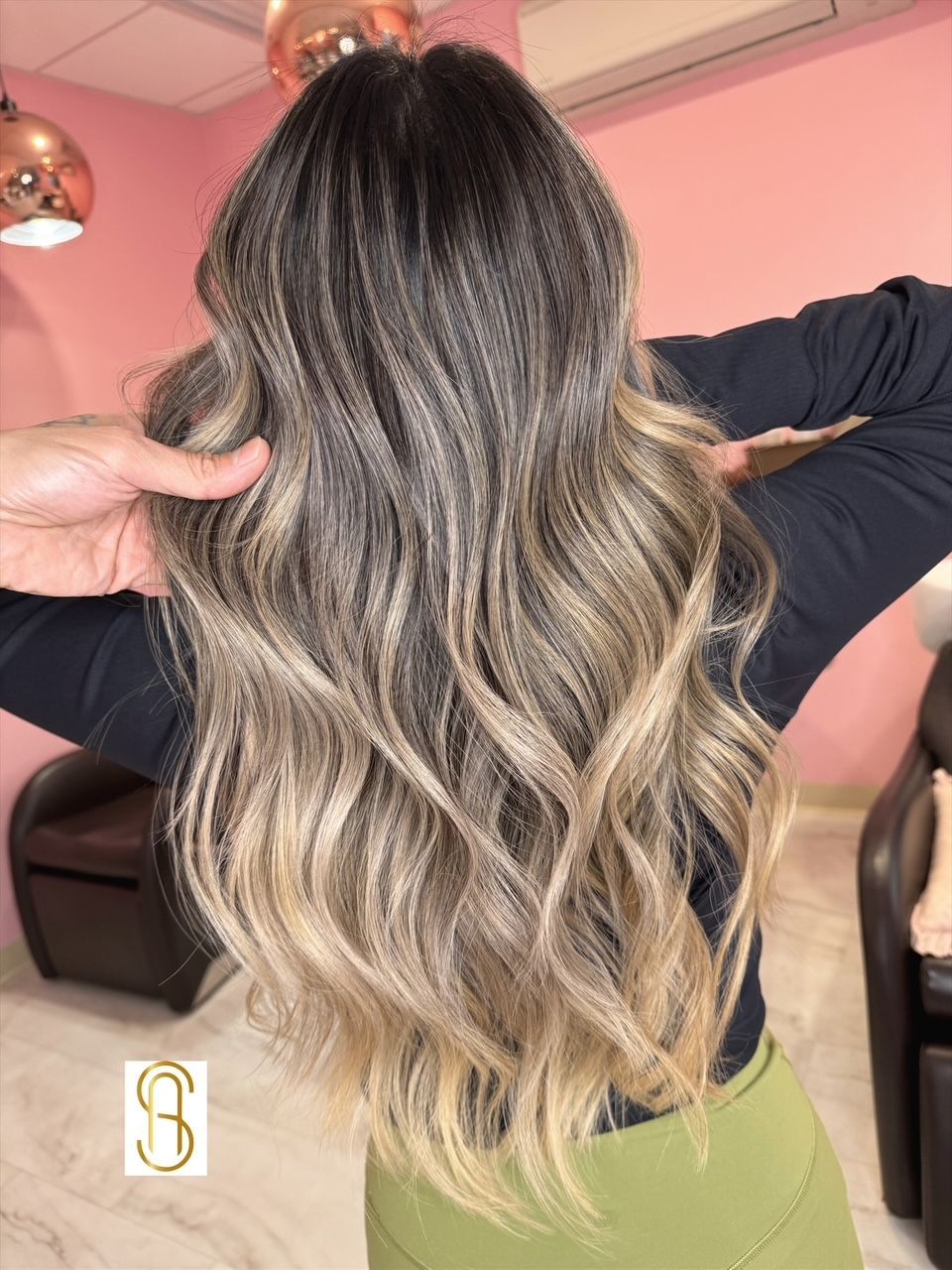 A woman with long wavy hair is standing in a room with her arms outstretched.