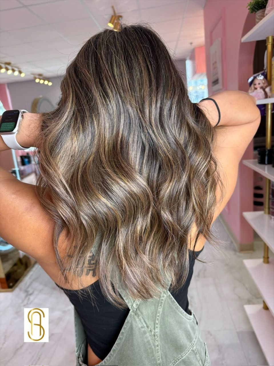 A woman with long brown hair is standing in a room with her hands behind her head.