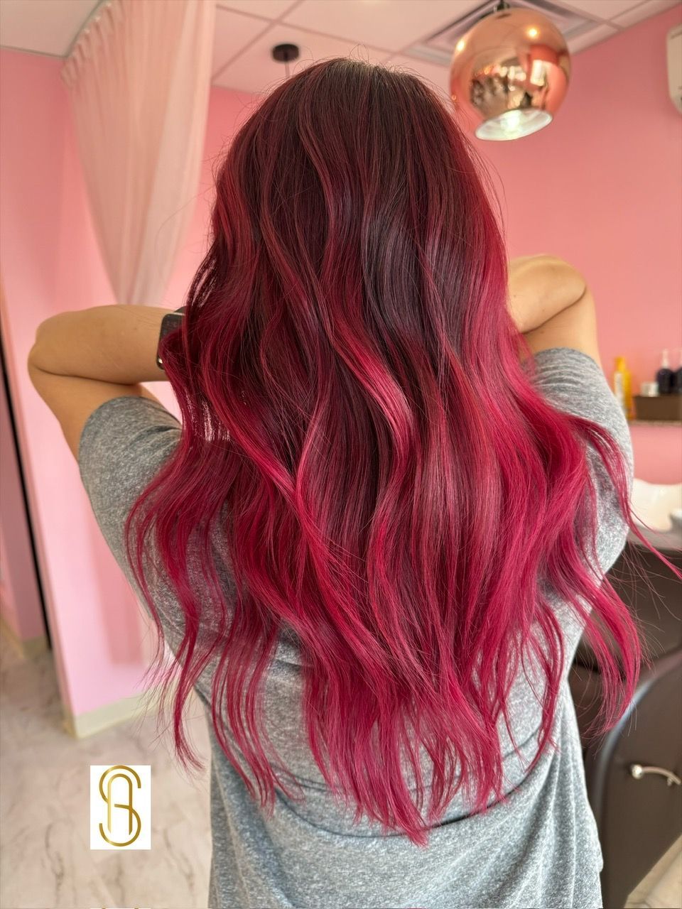 A woman with long red hair is standing in front of a pink wall.