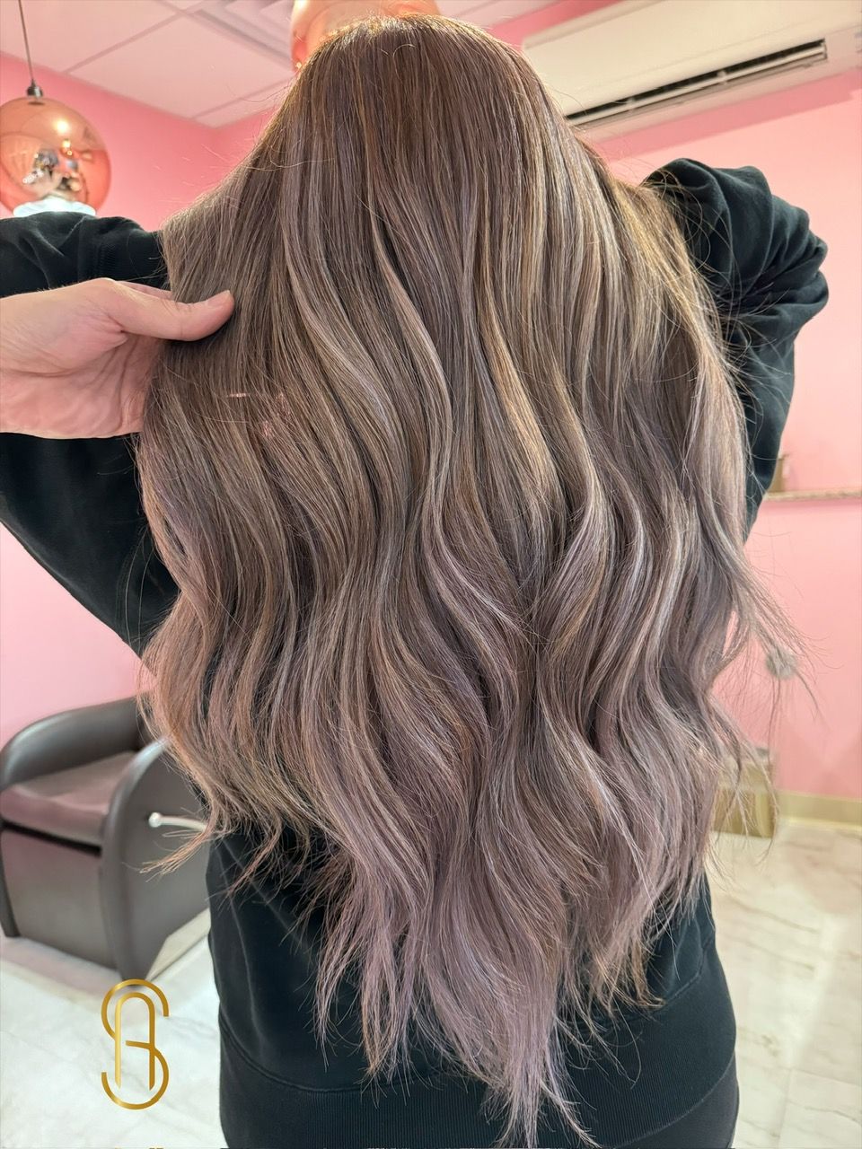 A woman with long wavy hair is standing in front of a pink wall.