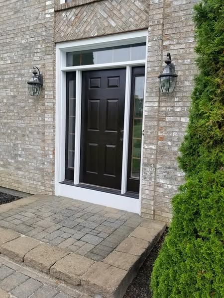 The front door of a brick house with a black door and white trim.