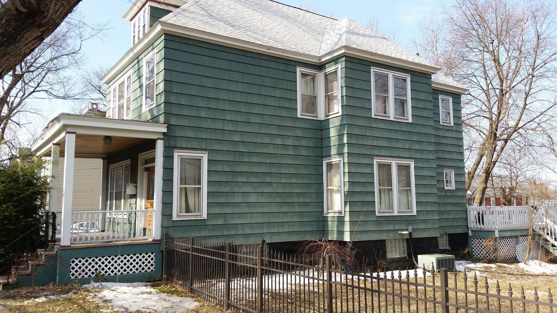 A green house with a porch and a fence in front of it