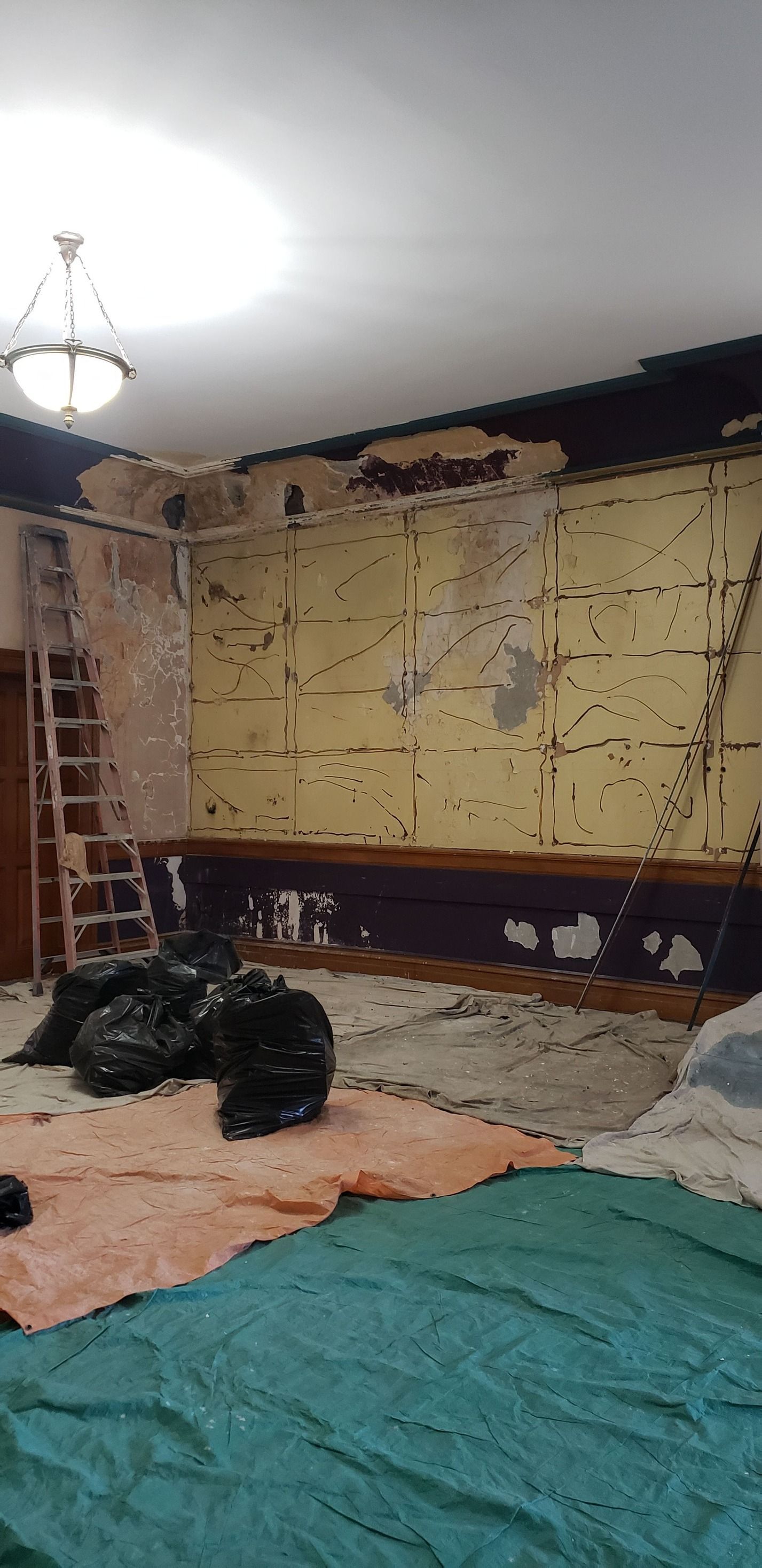 A room with a ladder and a green tarp on the floor.