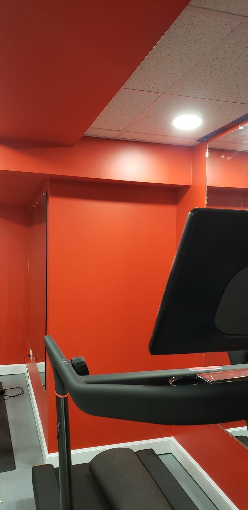 A treadmill in a gym with red walls and a mirror.
