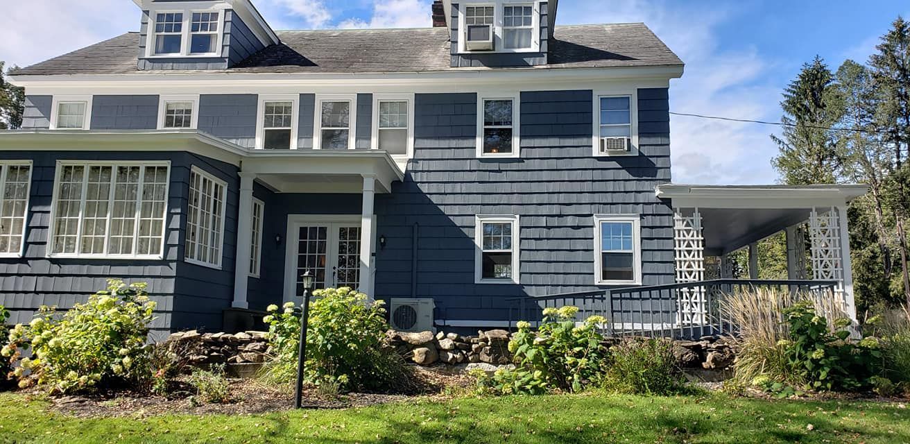 A large blue house with a porch and lots of windows is sitting on top of a lush green field.