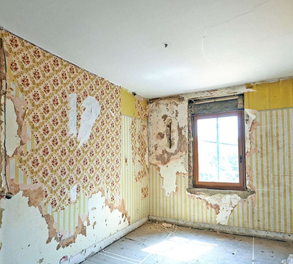 An empty room with peeling wallpaper and a window.