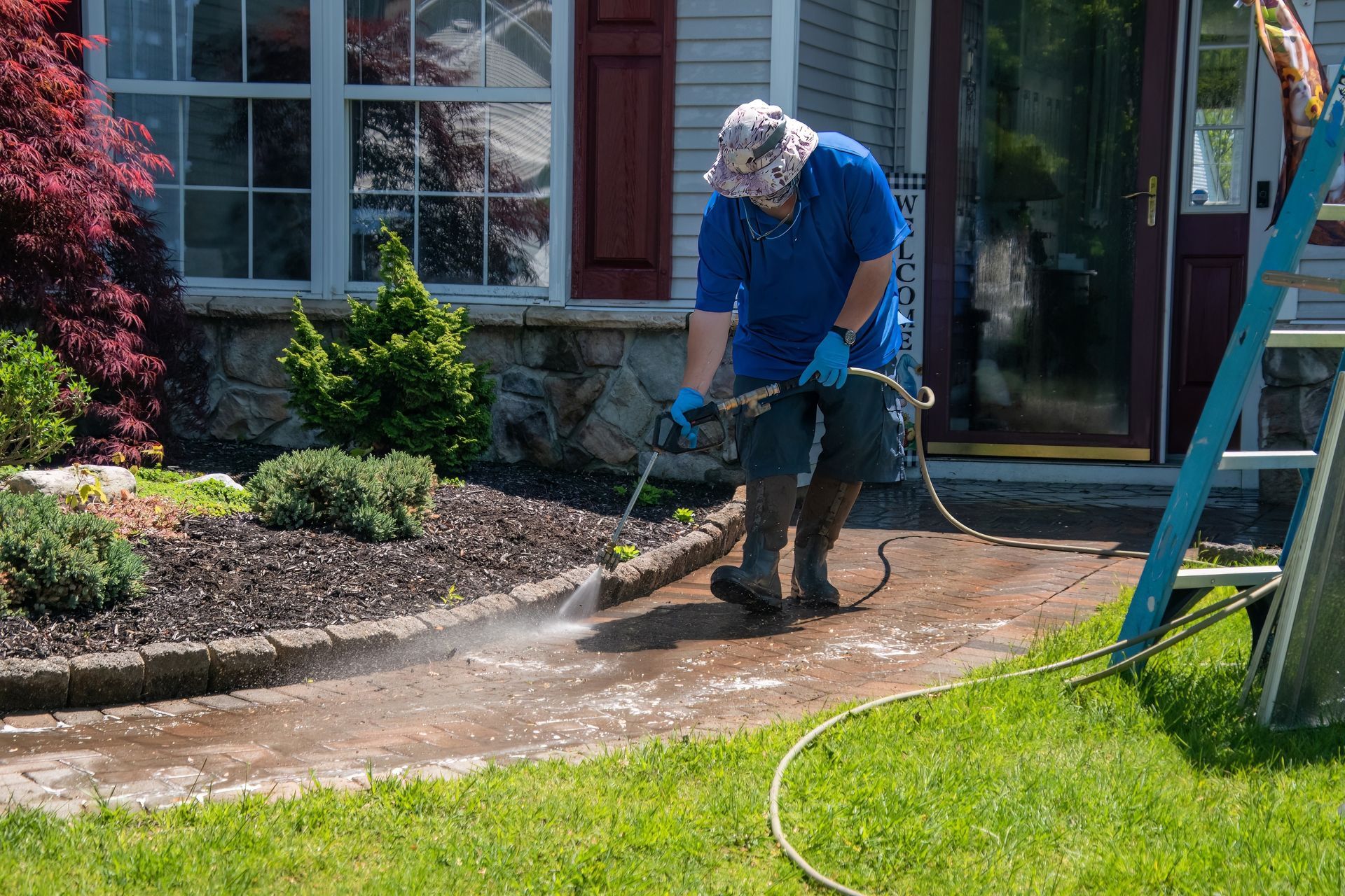 A man is using a pressure washer to clean a sidewalk in front of a house.