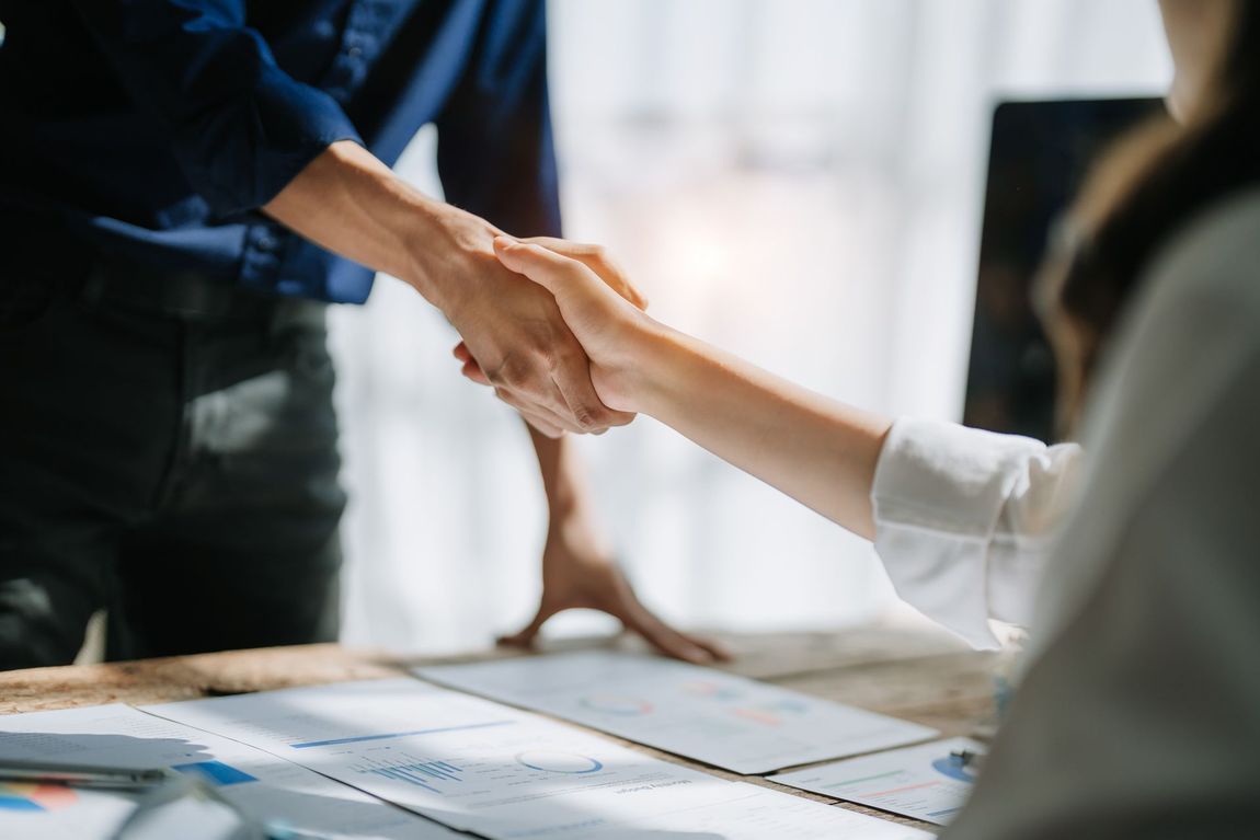 A man and a woman are shaking hands over a table.