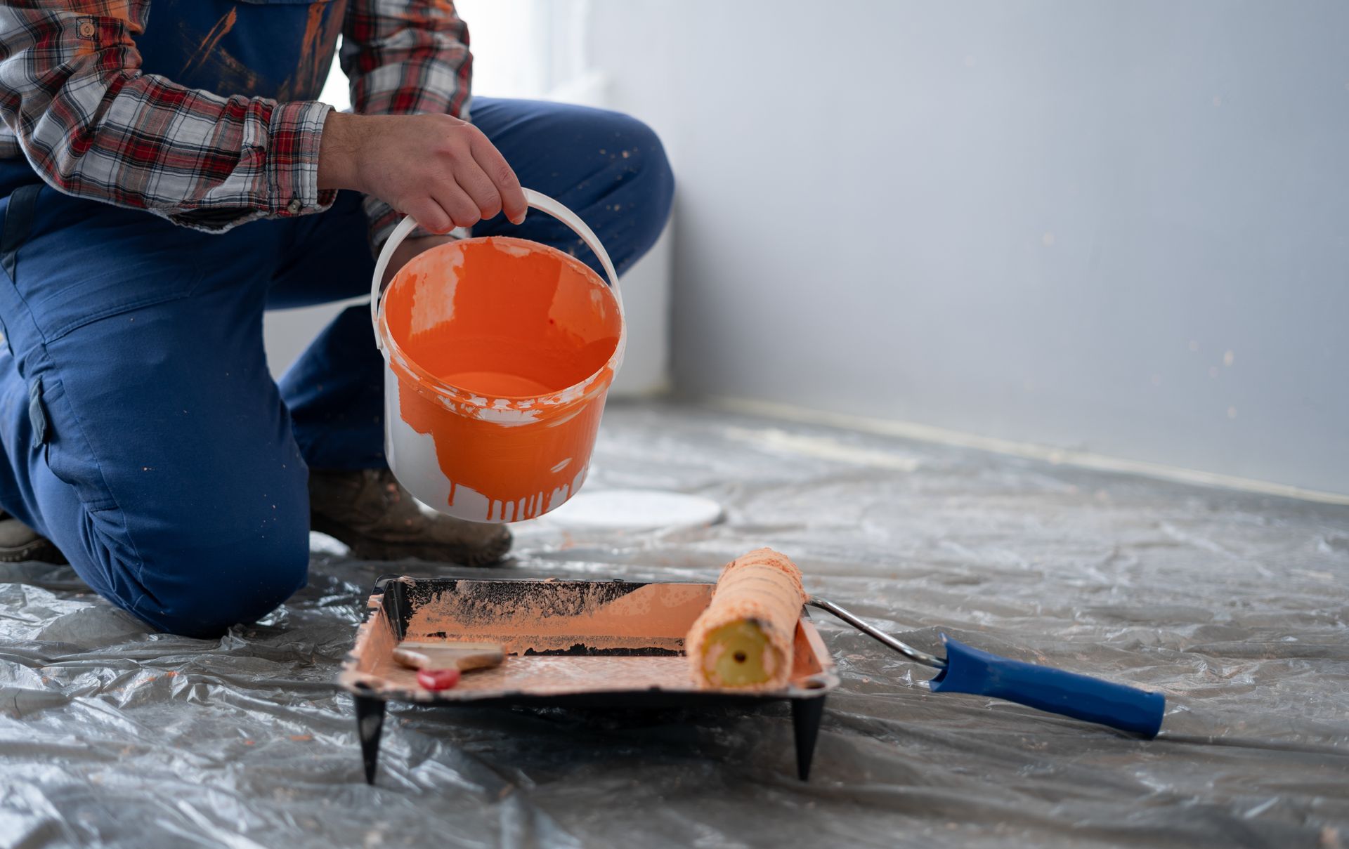 A man is kneeling down and pouring paint into a paint roller.