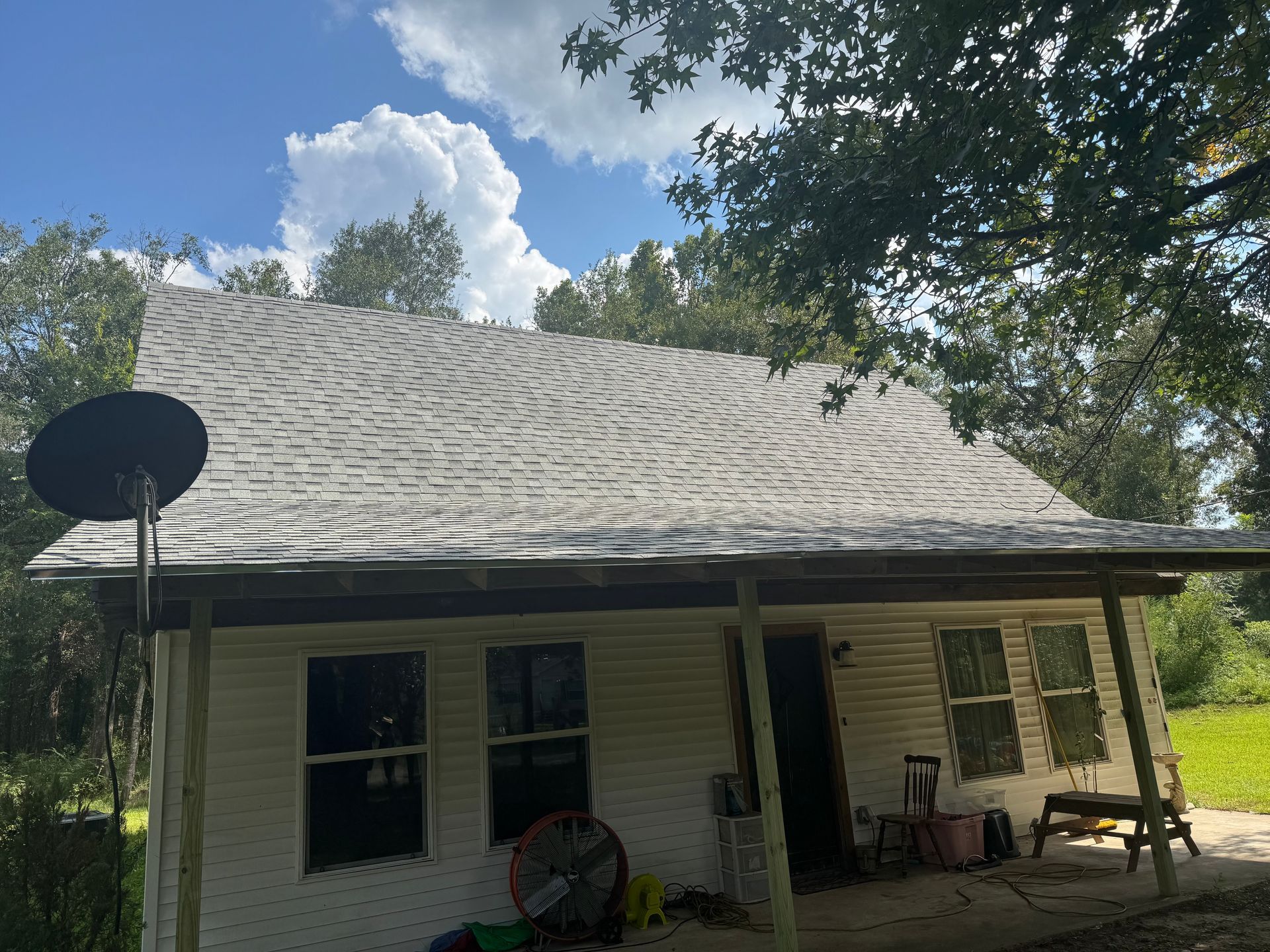 White house with gray shingled roof, satellite dish, trees in the background, cloudy sky.