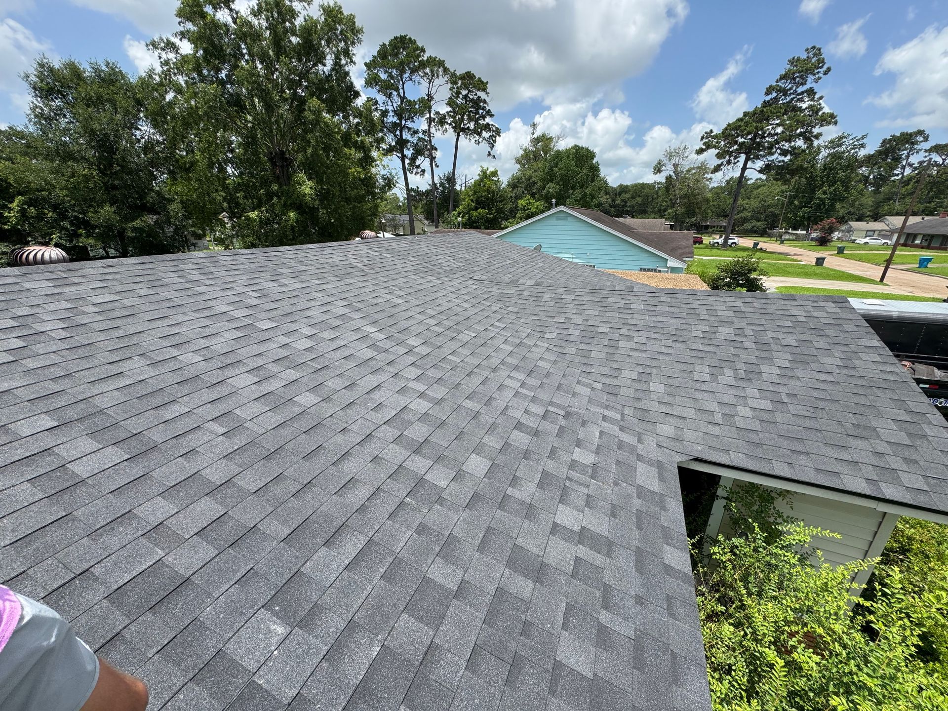 Gray shingle roof on a house with trees and blue sky in the background.