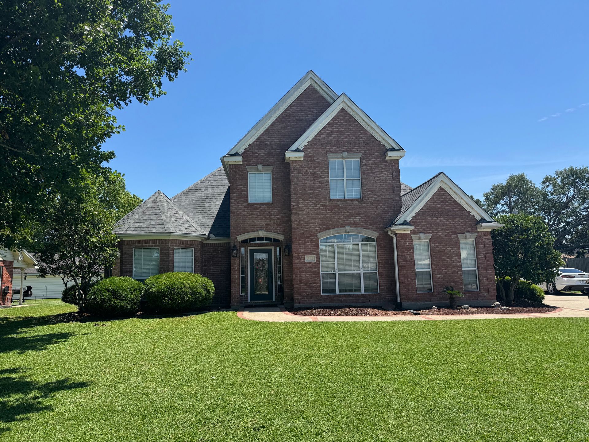 Two-story brick house with green lawn and blue sky.
