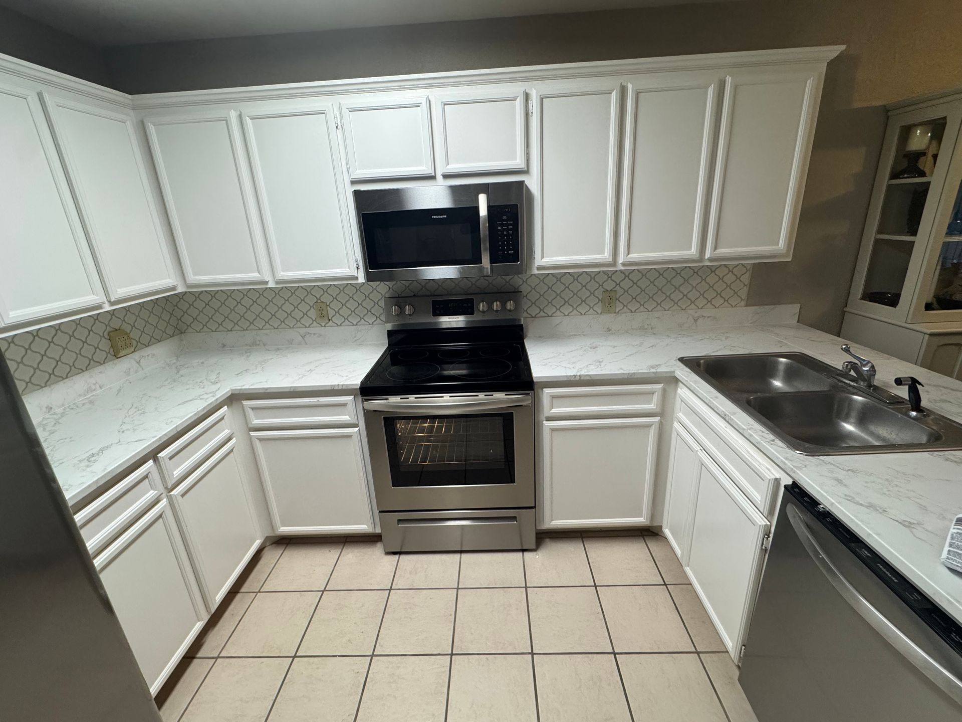 White kitchen with stainless steel appliances, white cabinets, and beige tile floor.