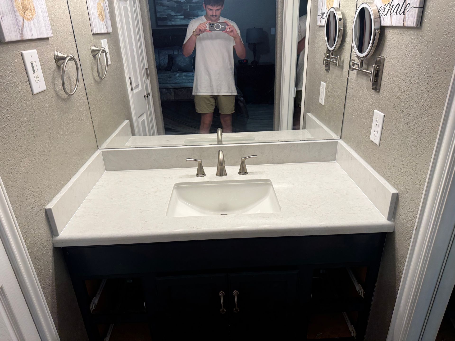 Bathroom with white countertop, dark blue cabinet, and a person taking a mirror selfie.