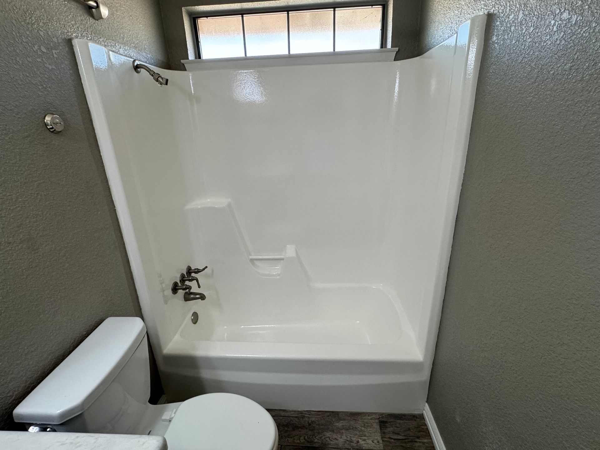 White bathroom with a shower/tub, toilet, and window. Gray walls.