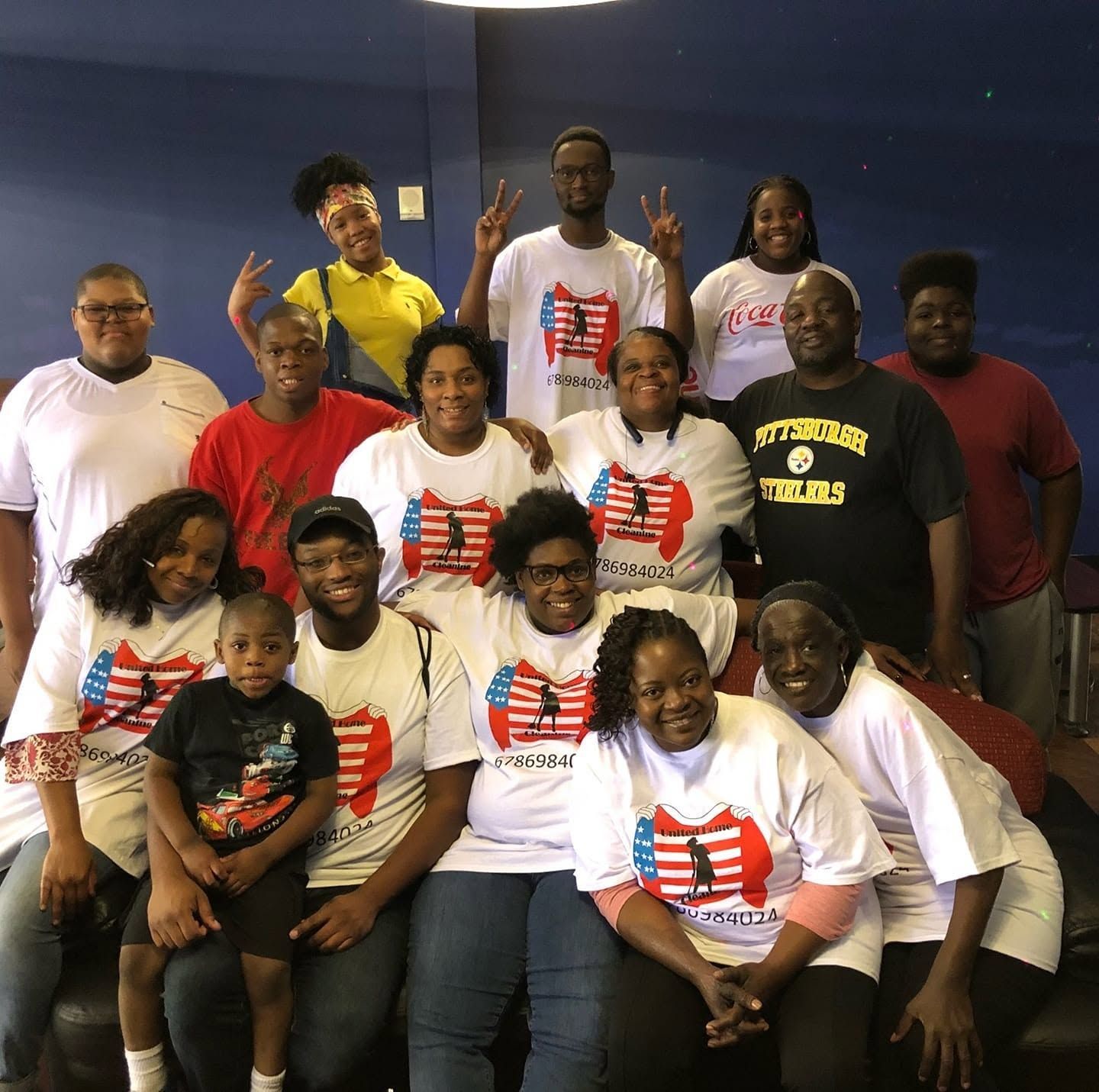 Group of people posing indoors in matching white shirts with red and blue designs, smiling and making peace signs