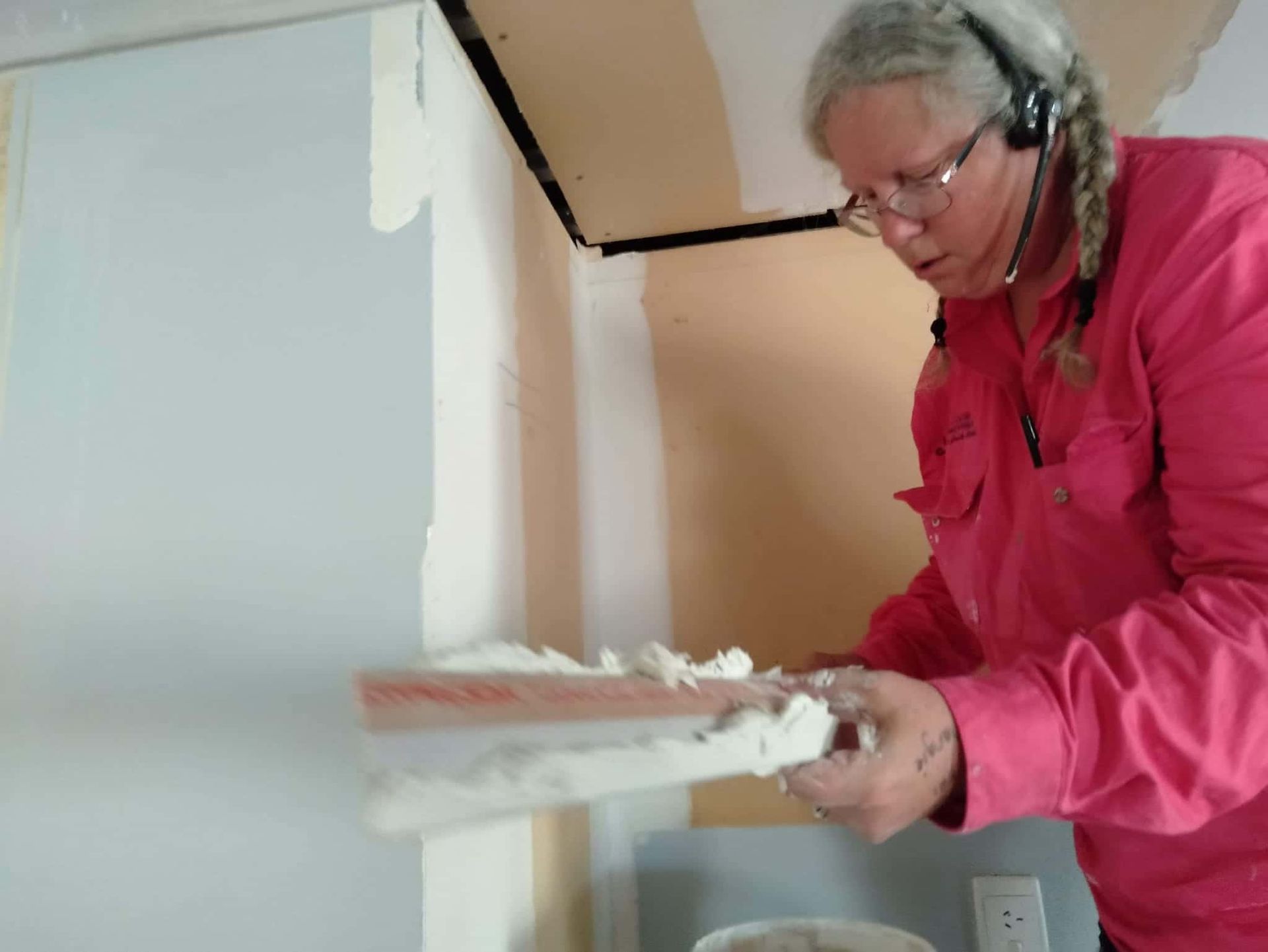 A Woman in A Pink Shirt Is Plastering a Wall — Your Local Handywoman in Burnett Heads, QLD