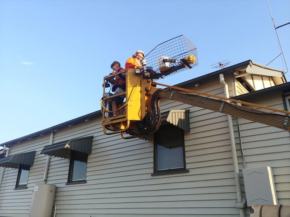 A Man in A Yellow Bucket Is Working on A Building — Your Local Handywoman in Burnett Heads, QLD