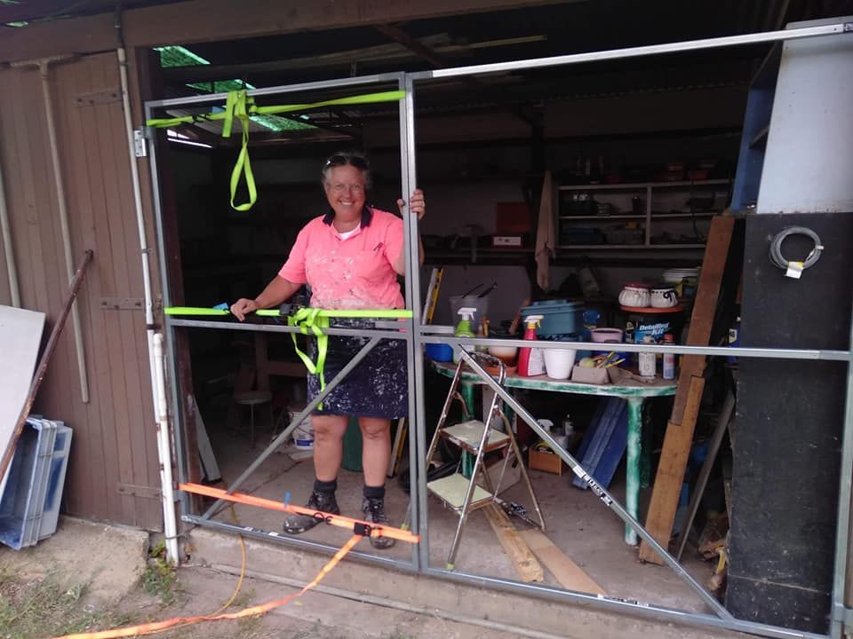 A Woman in A Pink Shirt Is Standing in Front of A Garage Door — Your Local Handywoman in Burnett Heads, QLD