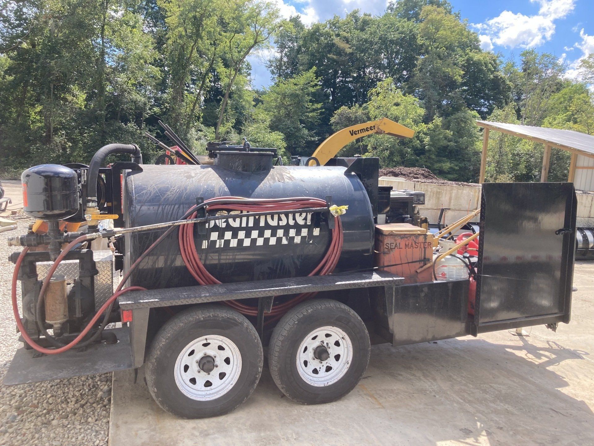 A black trailer with white wheels is parked in a dirt lot.