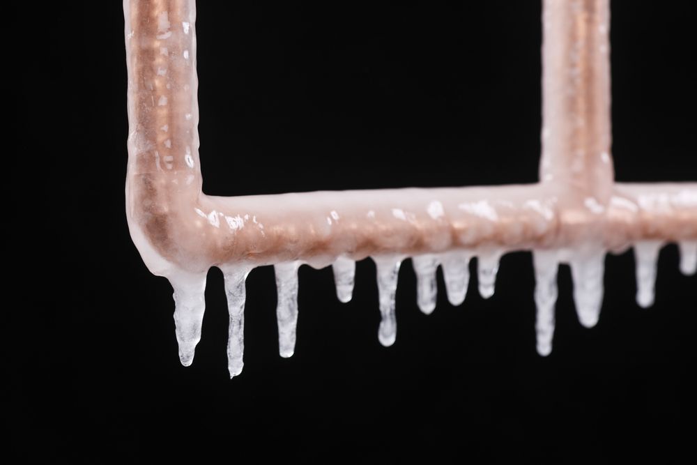 Icicles are dripping from a copper pipe on a black background.