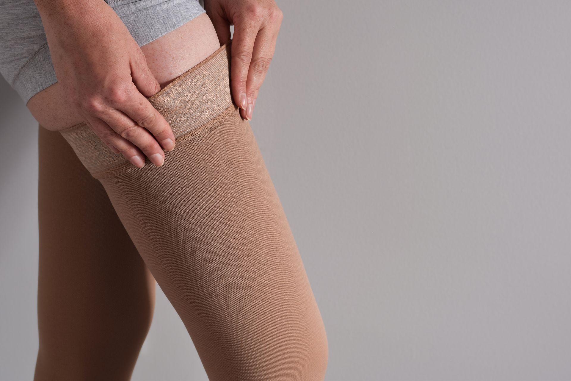 Person adjusting a tan compression stocking on their leg.