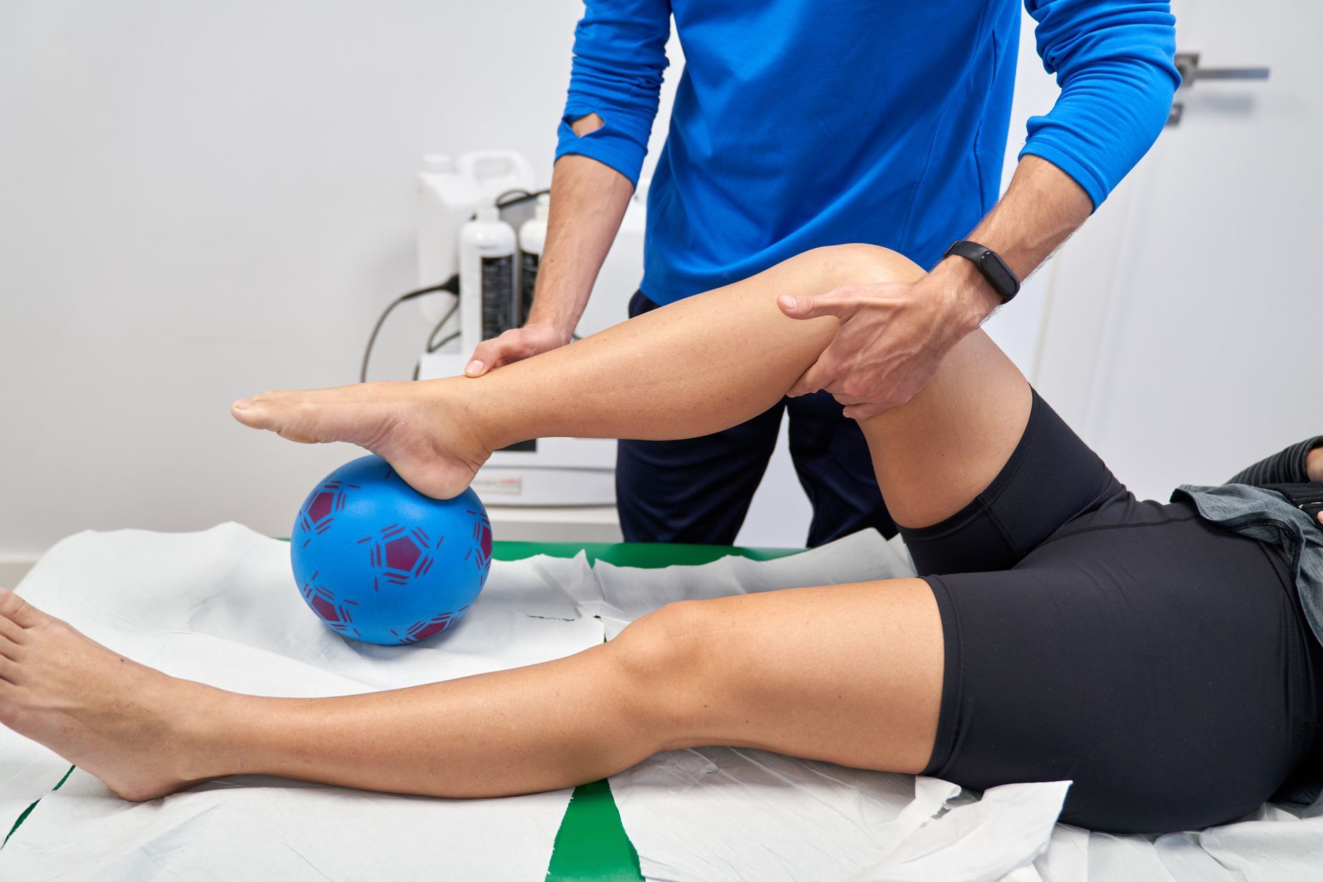 Therapist assisting a person with a leg exercise, using a blue ball for support.