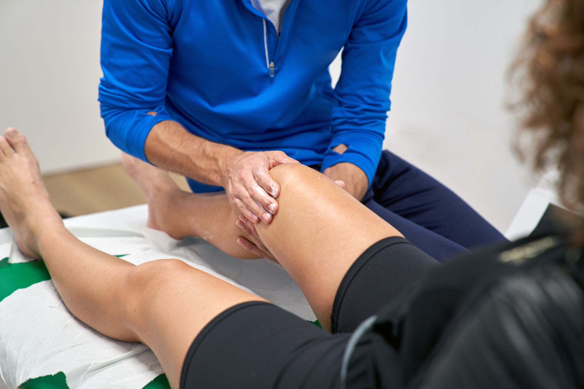 Woman assisting a man with arm exercise on a treatment table. Interior with neutral tones.