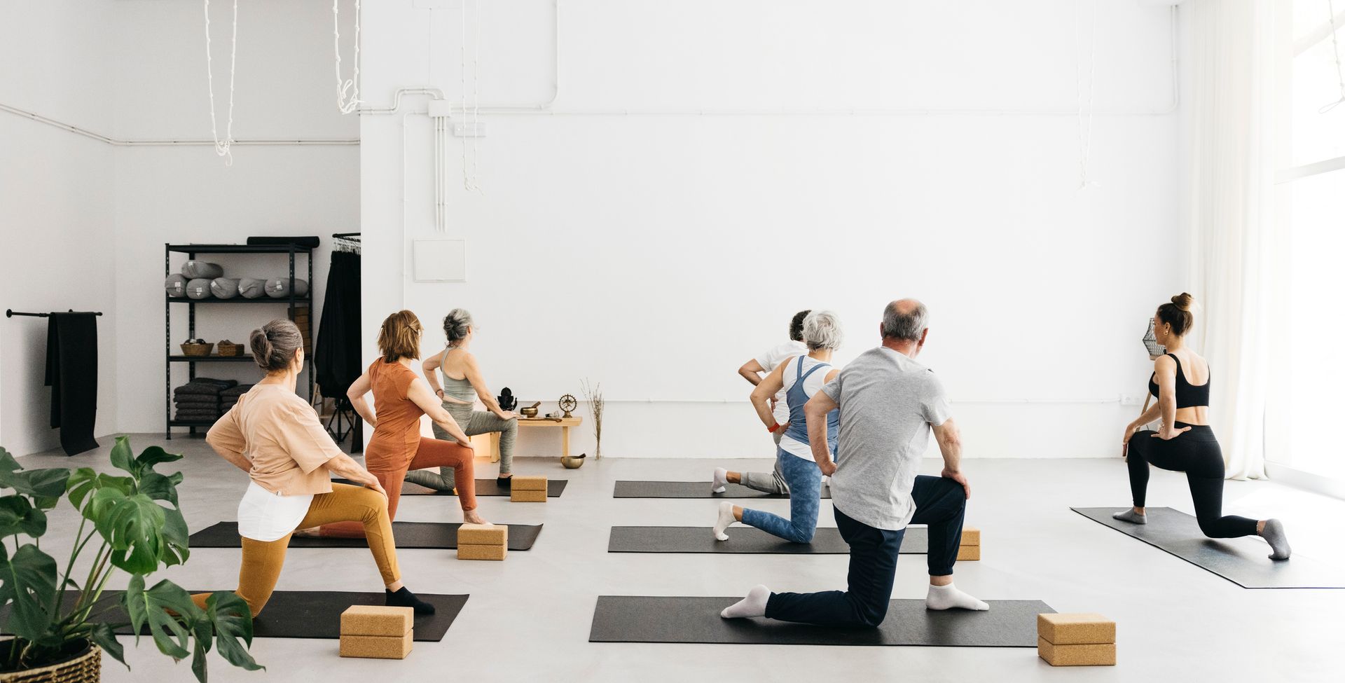 People in a bright studio doing a yoga class, led by an instructor.