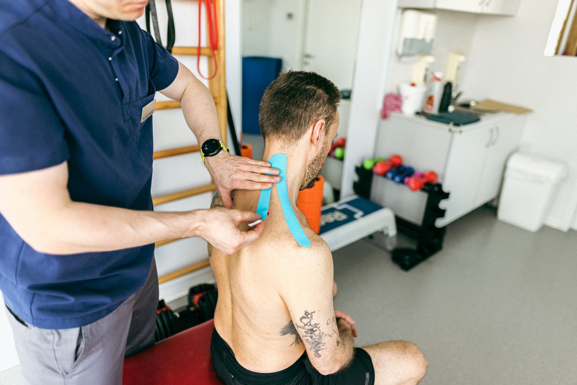 Man receiving blue kinesiology tape on his neck by another person in a clinic.