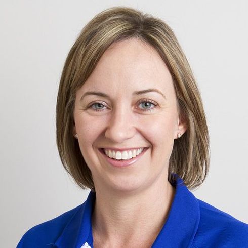 Woman with fair skin and brown hair, smiling, wearing a blue blazer.