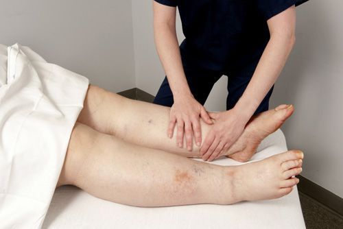Person giving a leg massage to another person lying on a white massage table.