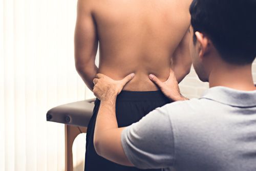 Physiotherapist examining a person's lower back, hands on hips, near a massage table.