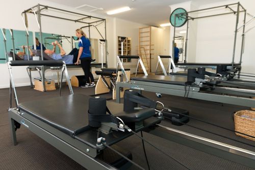 Pilates studio with equipment, instructor guiding a client using a reformer machine.