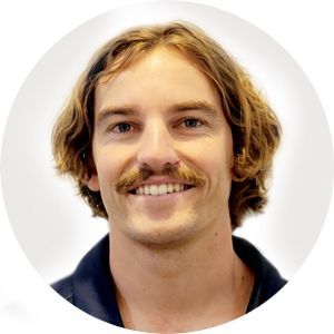 Man with wavy brown hair and a mustache smiles at the camera.