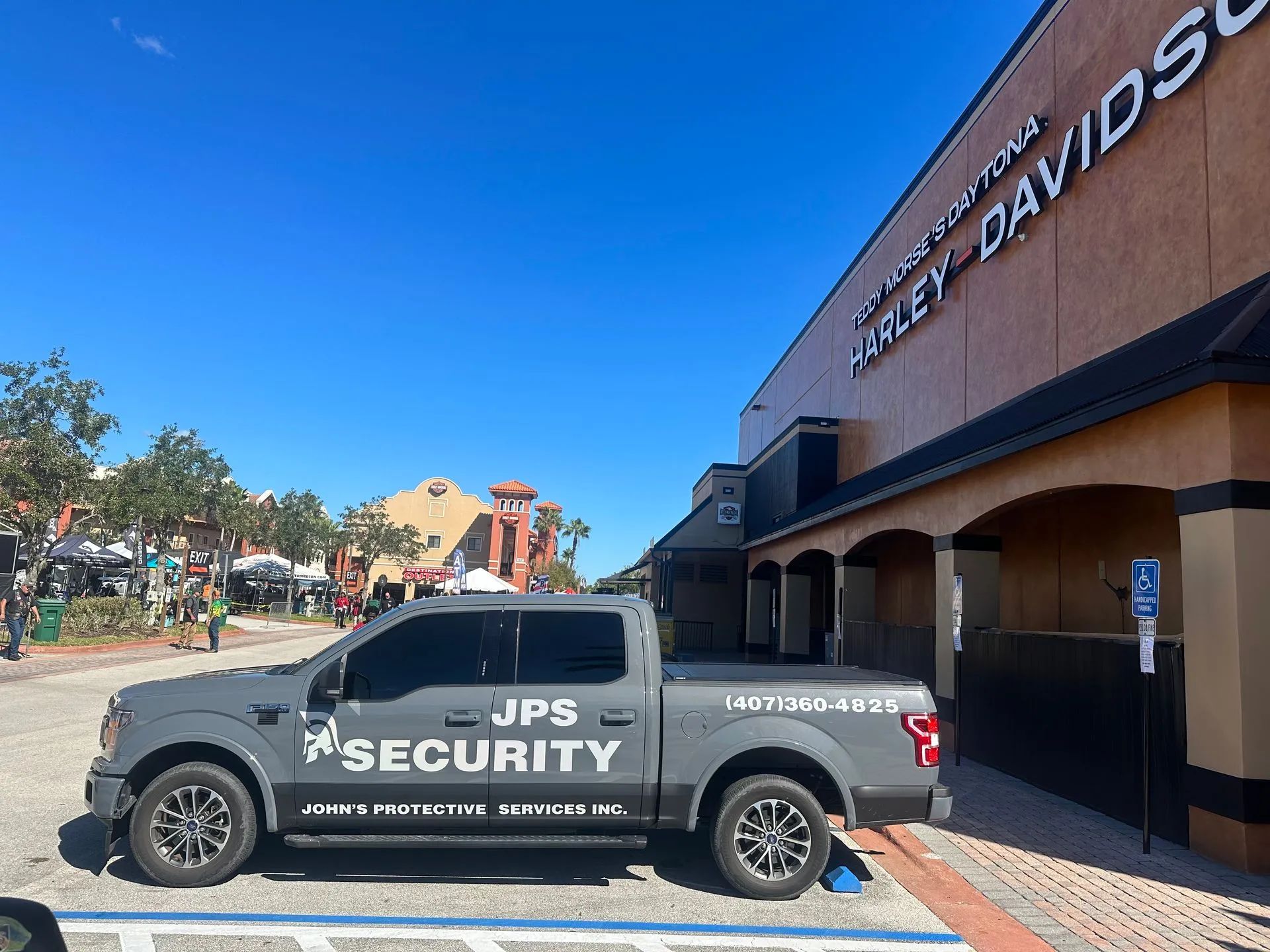 A JPS Security truck parked near a Harley-Davidson store on a sunny day.