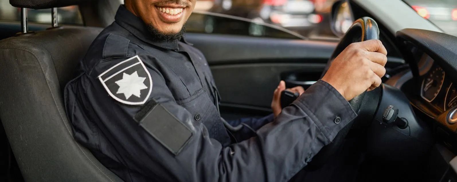 Smiling security guard driving a car in uniform, with a badge on the sleeve