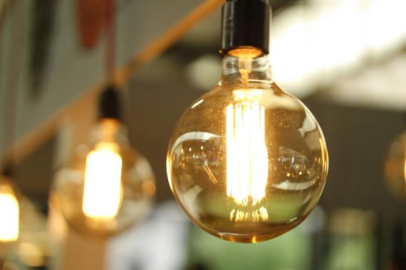 Close-up of a glowing, round lightbulb hanging from a dark cord. Others bulbs are blurred in the background.