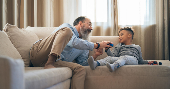 Grandfather and grandson playing on a beige couch, smiling in a living room.