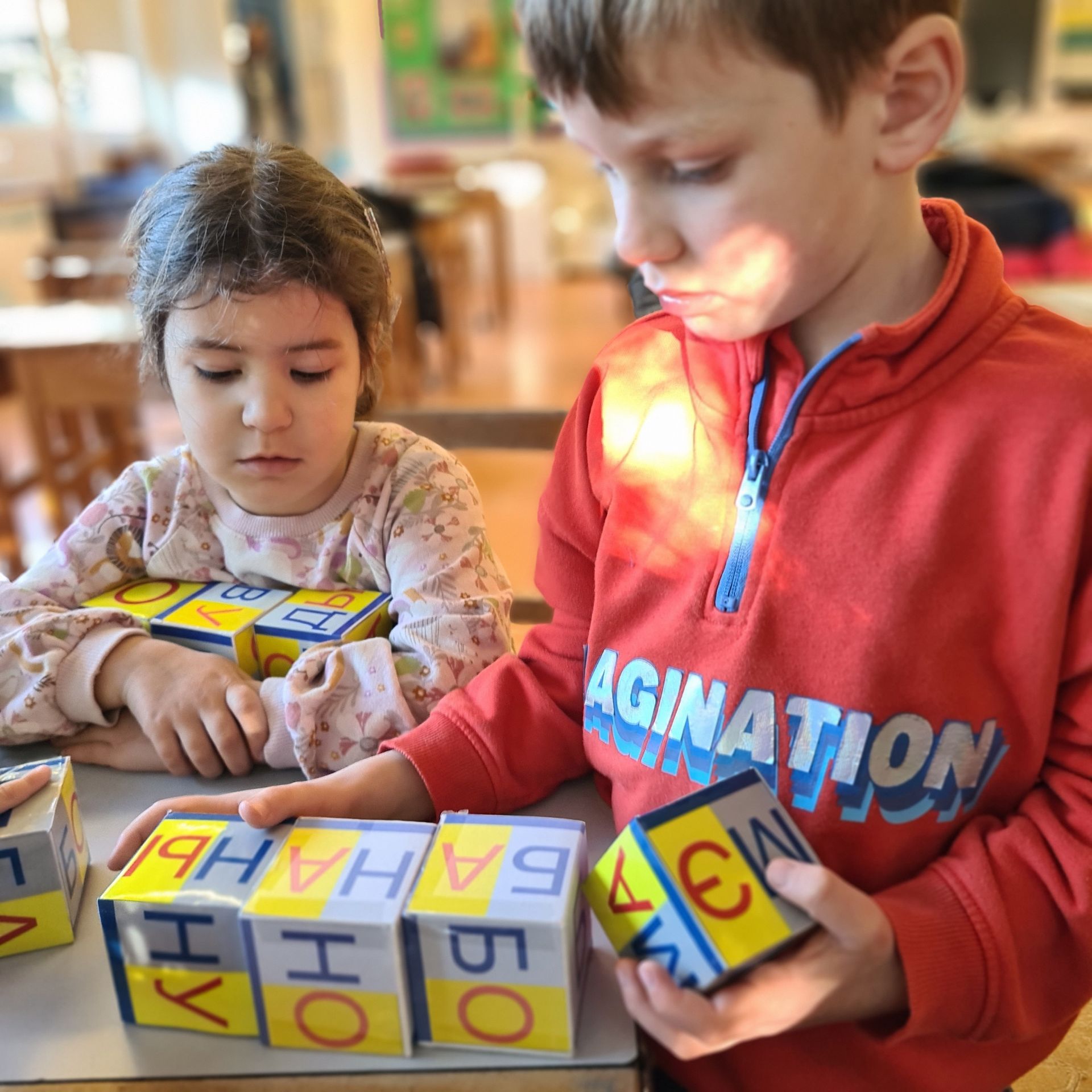 Мальчик в красной толстовке с надписью «Agination» играет с кубиками