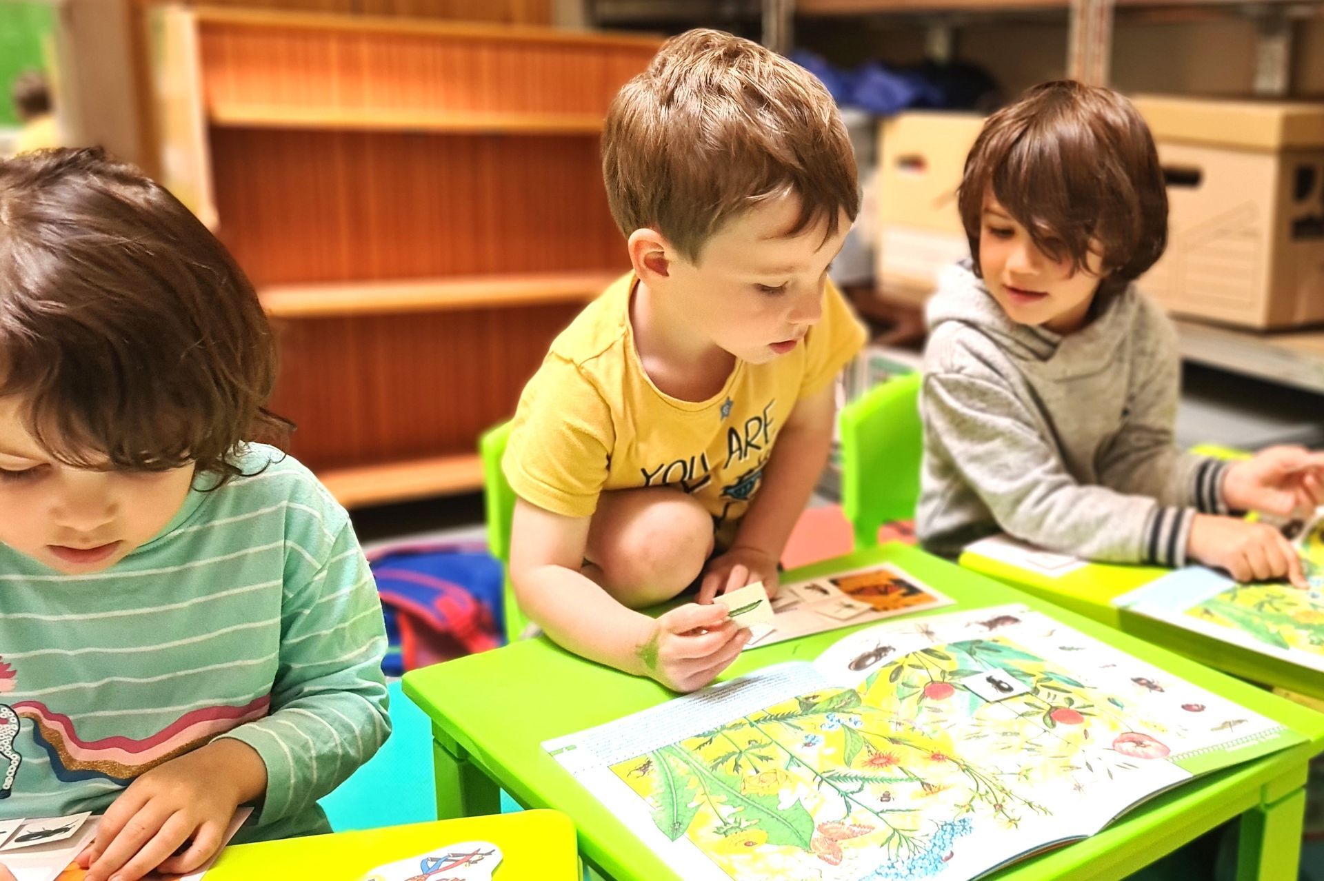 Трое детей сидят за зеленым столом и рисуют.