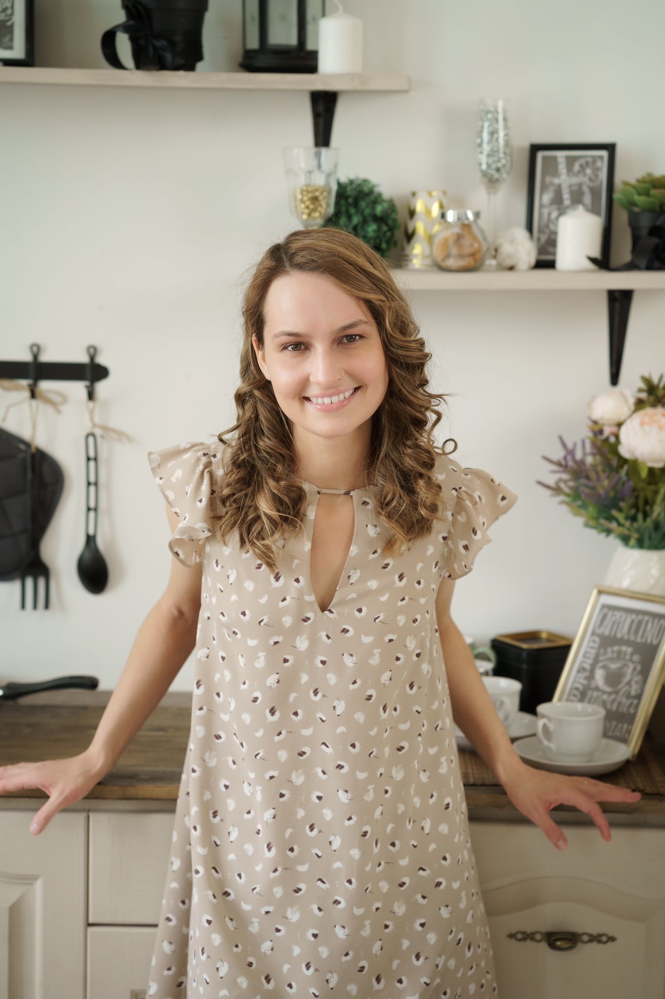 Женщина в платье стоит на кухне, опираясь на стойку.