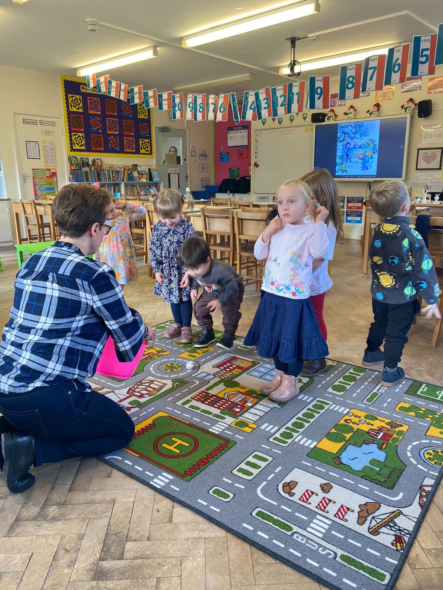 Группа детей стоит на ковре в классе.