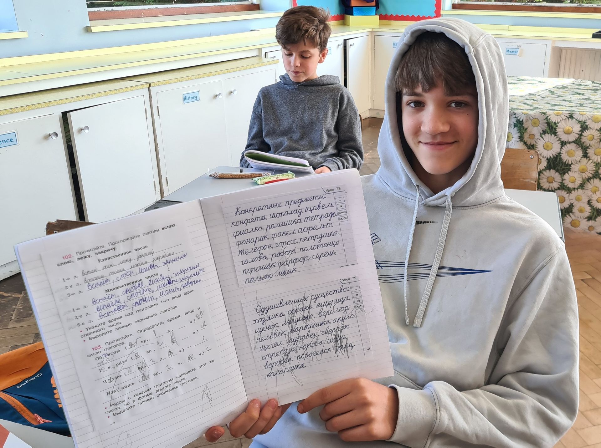 Мальчик в толстовке с капюшоном держит листок бумаги с надписью.