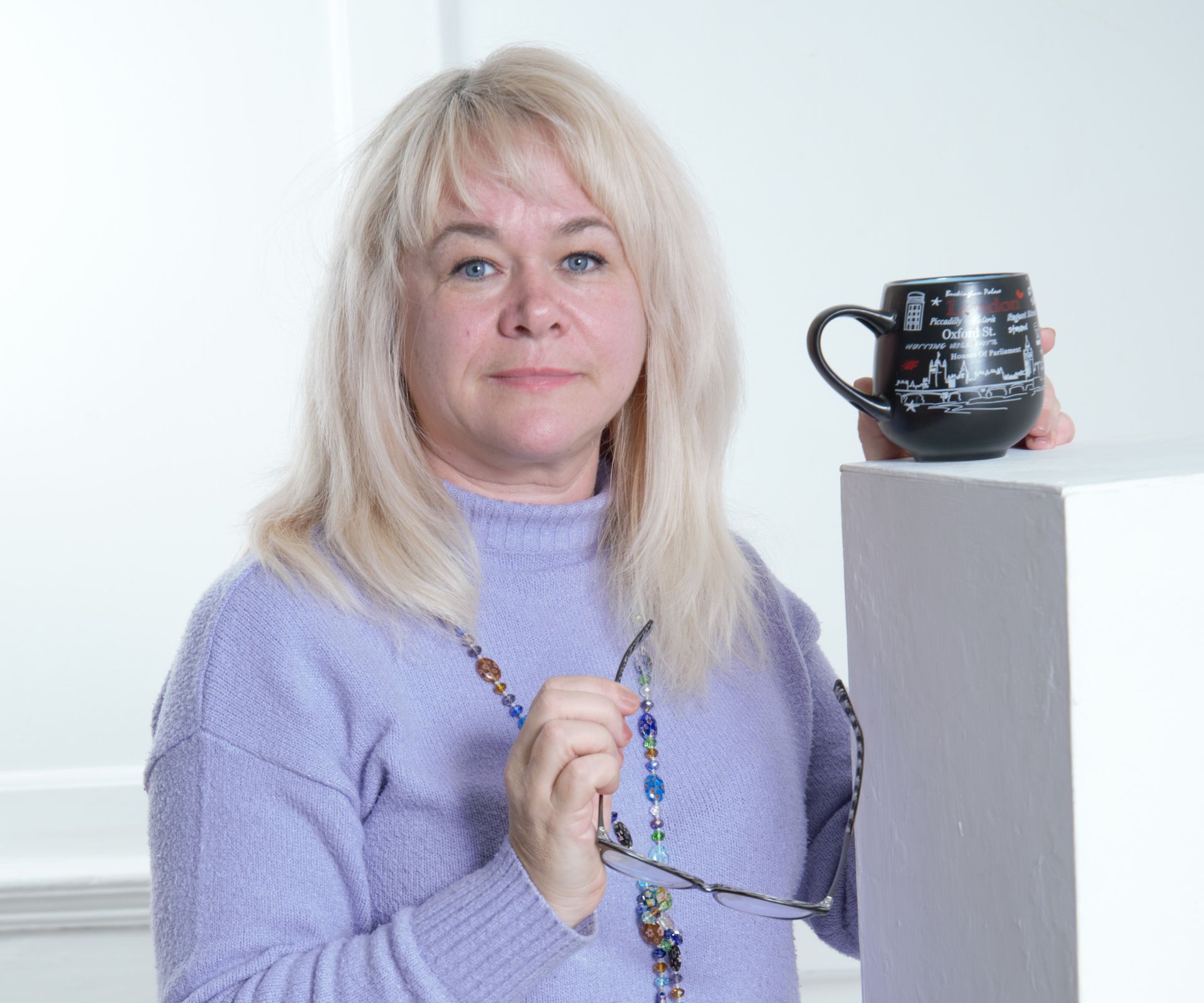 Женщина в фиолетовом свитере держит чашку и стаканы.