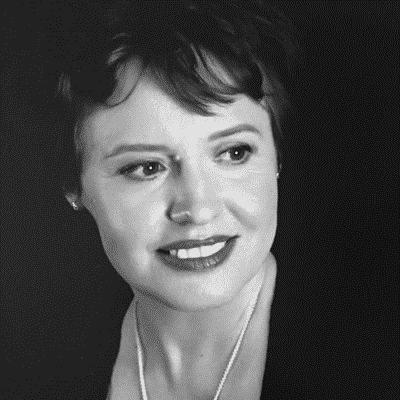 Черно-белая фотография женщины с ожерельем на шее и улыбкой.